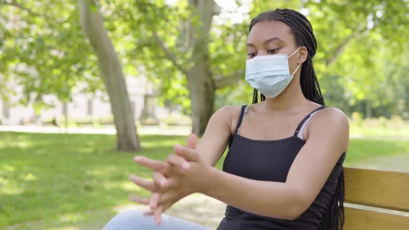 A Young Black Woman in a Face Mask Applies Disinfection Gel on Her Hands and Looks at the Camera