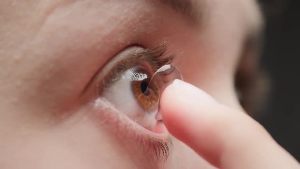 Closeup of a Browneyed Young Woman Putting on the Contact Lens with Fingers and Blinking