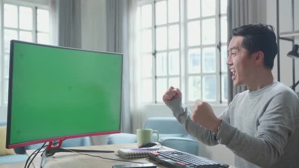 Asian Man With Green Screen Desktop Computer Being Happy Successful While Working At Home