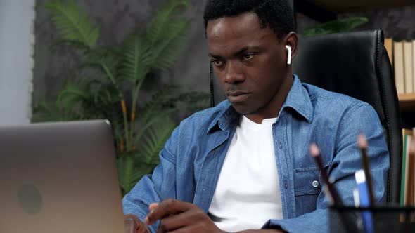 African American Man in Wireless Earphones Works for Laptop Typing on Keyboard