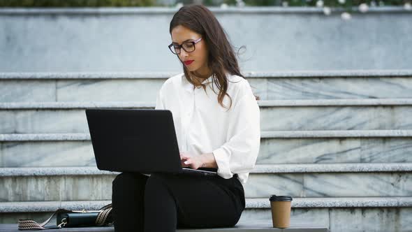 Girl in Glasses and Formal Attire Sitting on Bench Stairs and Typing on Laptop Computer Working