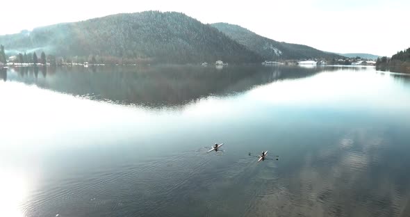 4K low drone shot over winter lake in French mountainswith two kayaks paddling in the sun. A sungla