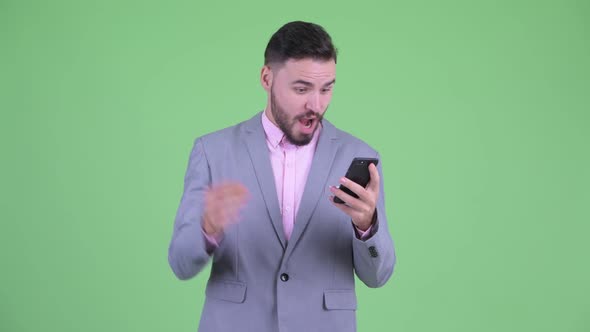 Happy Young Bearded Businessman Using Phone and Getting Good News