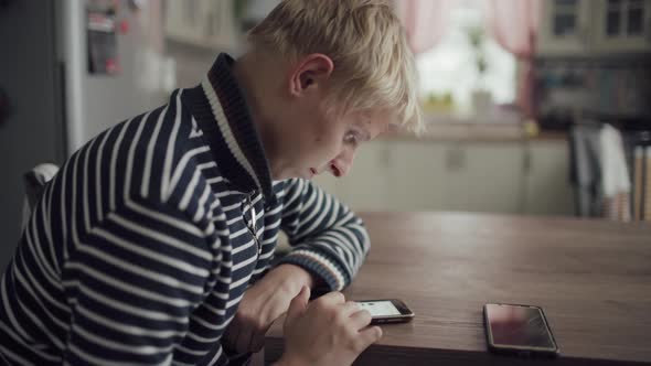 Young Blond Man Sits Kitchen Home And Uses Smartphone For Communication