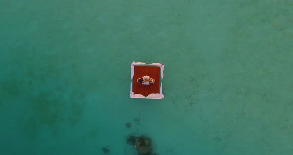 Aerial drone view of a man and woman having dinner on a floating raft boat at sunset