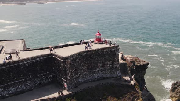 Breathtaking aerial pan view around famous clifftop Farol da Nazare lighthouse.