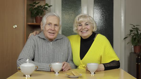 Happy Old Grandparents Couple Sit on Table at Home Enjoy Drinking Tea Together