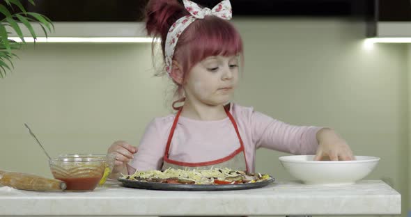 Cooking. Little Child in Apron Adding Grated Cheese To Raw Pizza in Kitchen