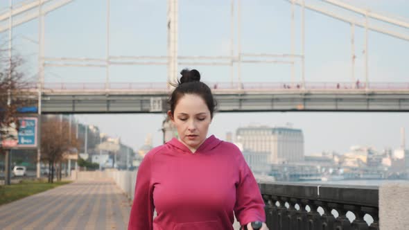 Nordic Walking, Young chubby lady with nordic walking poles training along city river and bridge