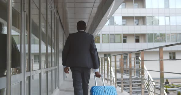 Back View of African Businessman Walking with Suitcase Outside Airport