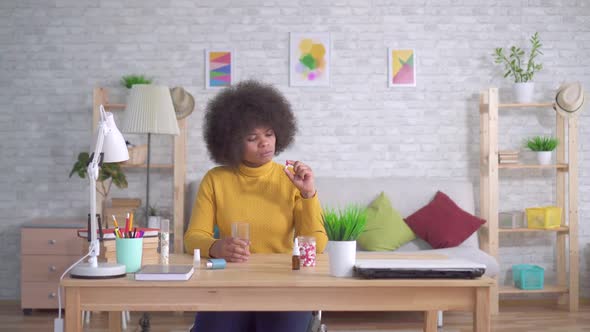 Beautiful African American Woman with an Afro Hairstyle Takes a Pill and Drinks From a Glass of