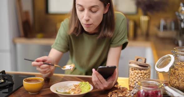 Woman with Coffee and Phone on the Kitchen in the Morning