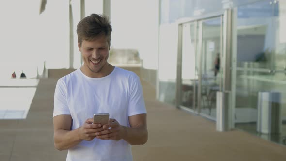 Smiling Bearded Guy Walking with Smartphone Near Modern Building