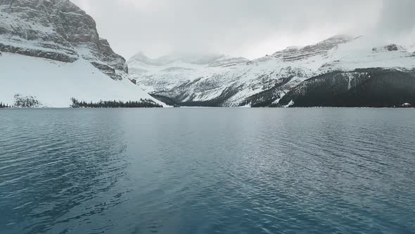 Aerial footage of the surface of Bow Lake with snow-capped mountains in Alberta, Canada