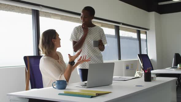 Two diverse female colleagues looking at laptop and discussing in office