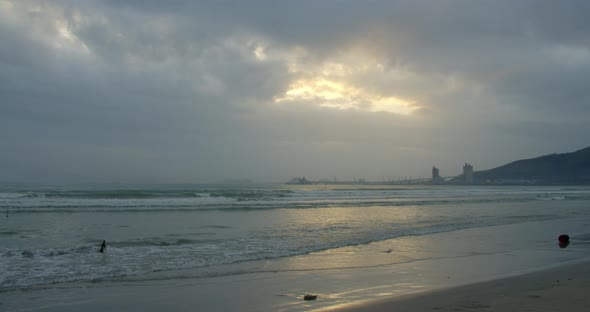 A Large Sun Appears From Behind the Clouds and Large Mountains Touch the Horizon and Coast