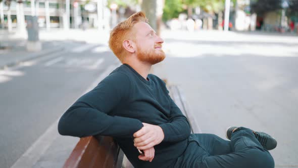 Relaxed ginger man looking around while sitting on the bench