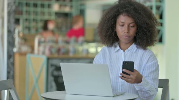 African Businesswoman Using Smartphone and Laptop in Cafe