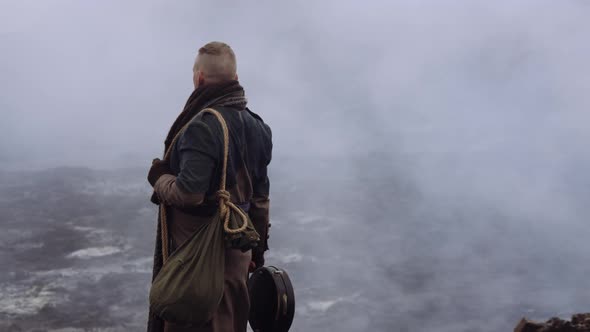 Man In Greatcoat Standing In Misty And Rocky Landscape