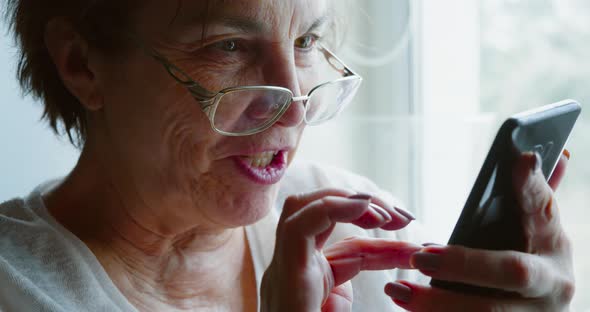 Closeup of an Elderly Woman Receives a Funny Message on Her Smartphone and Laughs Happily