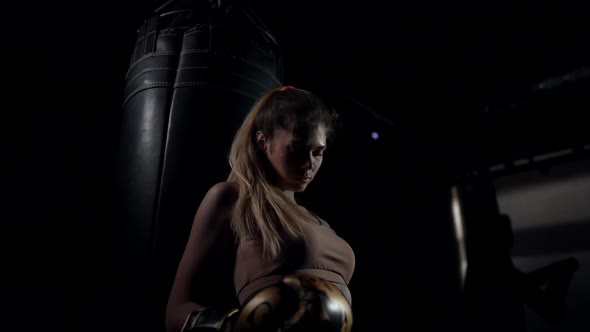 Bottom Angle View of Confident Satisfied Young Female Boxer Leaning on Punching Bag Looking Away