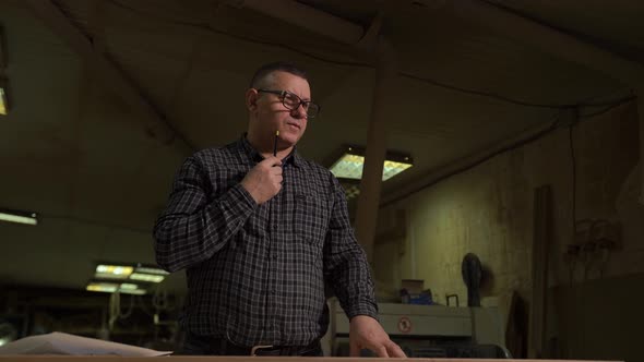 Engineer in Shirt Stands Against Background of Production with Sketch on Paper