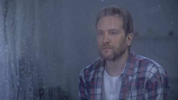 Lonely Man Looking at Camera Through Window on Rainy Day, Depression Problems