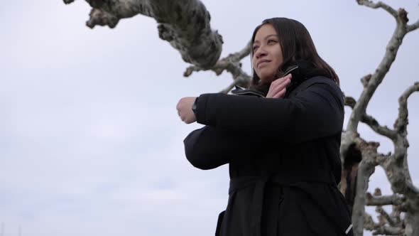 Young attractive woman crosses her arms and enjoys the stylish silent winter atmosphere on a tree