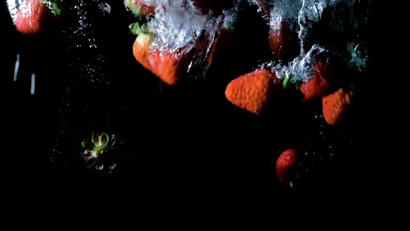 Strawberries dropped into water on black background, slow motion close up