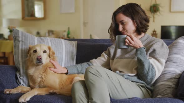 Smiling caucasian woman stroking her pet dog sitting on sofa at home