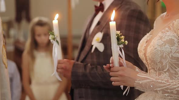 Bride and Groom Stand in Church at Christianity Wedding Ceremony Holding Candles in Their Hand