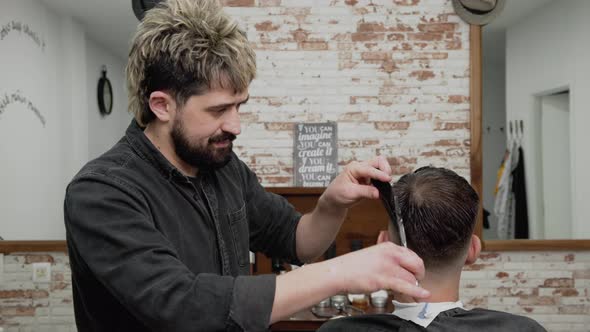 Barber Cutting Hair with Scissors to a Handsome Young Man