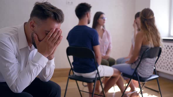 Group Therapy Session, Sad Man Covers His Face with Hands on Background of People Sitting on Chairs