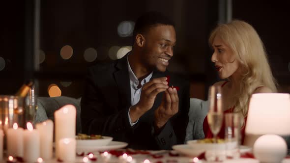 African Man Making Proposal To Girlfriend Showing Ring In Restaurant