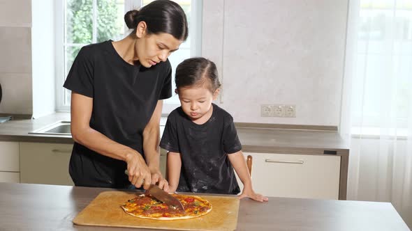 Mom Cuts Freshly Baked Pizza in Front of Little Daughter