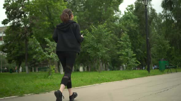 A Young Woman is Jogging with Her Phone in the Park