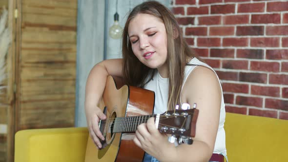 Woman is Sitting on Sofa Playing Guitar and Singing Side View