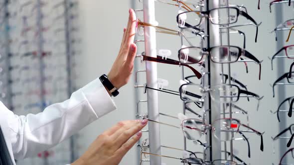 Eyesight concept. Woman standing near the stand with stylish eyeglasses in the optical store. Buyer 