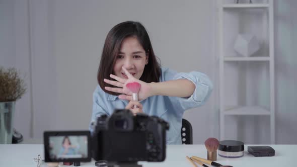 asian woman or beauty blogger with brush and camera recording video and waving hand at home.