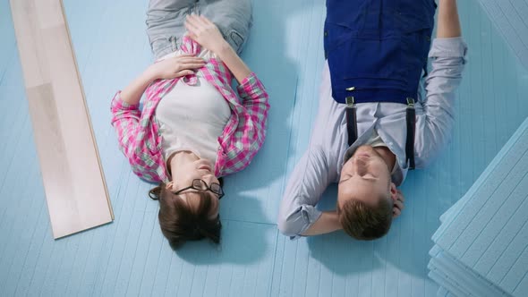 Man and Woman Lying on Expanded Polystyrene Floor Rejoicing at Job Done While Installing Laminate