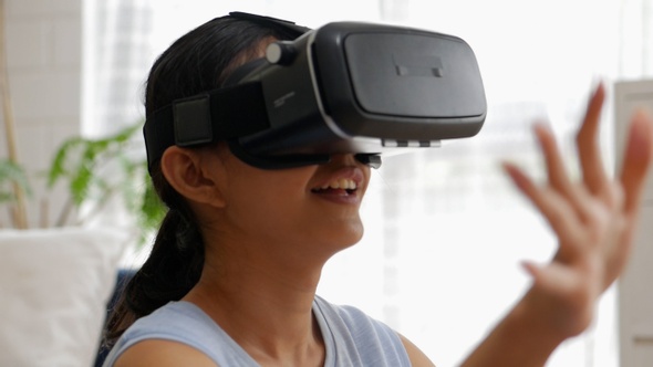 Portrait of a young Asian woman using a virtual reality headset in the living room at home.