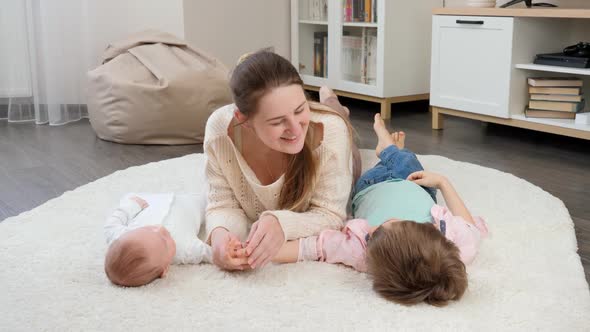 Cute Baby and Older Boy Lying with Smiling Mother on Carpet in Living Room