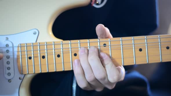 Person playing a solo on a cream white electric guitar. Static frontal close up view