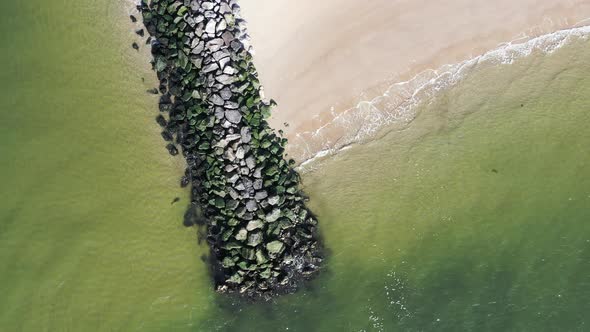 A top down drone view of a stone jetty as the ocean waves gently crash onto the shore. The camera lo