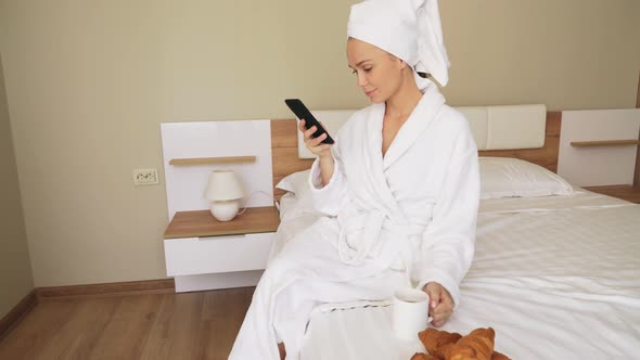 Girl Using Phone, Drinking Coffee on Bed.