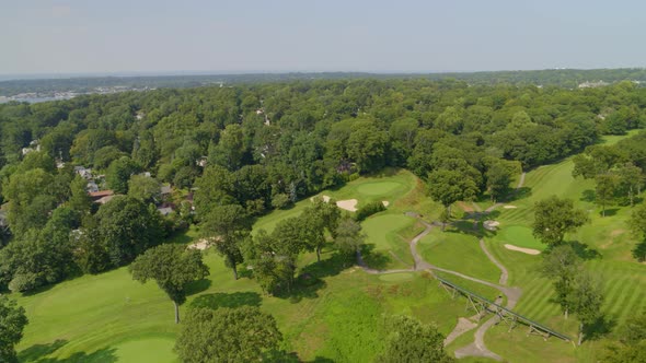 Flying Over Golf Course and Towards Small Town Amongst Trees and Near Water