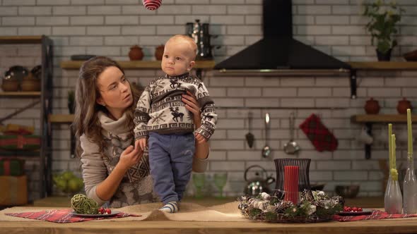 Pretty Young Woman and Cute Baby in Her Arms Standing in Modern Kitchen