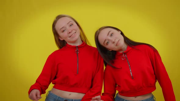 Smiling Young Women Moving Simultaneously Dancing at Yellow Background Looking at Camera