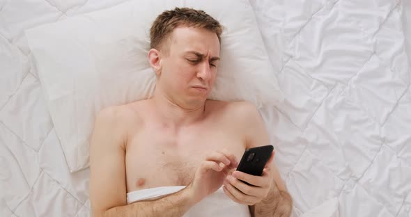Young Man Lies in Bed with Phone Reads the News and is Surprised