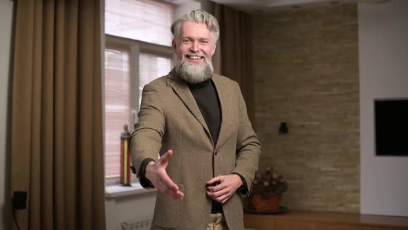 Adult gray-haired man with beard smiles and holds out his hand in greeting